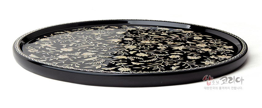 [텍스트: 샵오브코리아 대한민국의 품격까지 전합니다] 검은 옻칠 바탕 위 자개 상감으로 넝쿨과 꽃문양을 섬세하게 표현한 원형 나전칠기 쟁반 모습