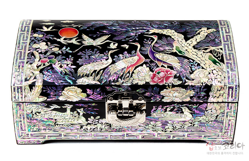 [텍스트: 샵오브코리아 대한민국의 품격까지 전합니다.] 흑색 옻칠 바탕 위 자개 상감 기법, 송학과 소나무·모란 문양, 오방색 계열 화려한 색채와 금속 장식 잠금장치가 어우러진 곡선형 보석함 디자인
