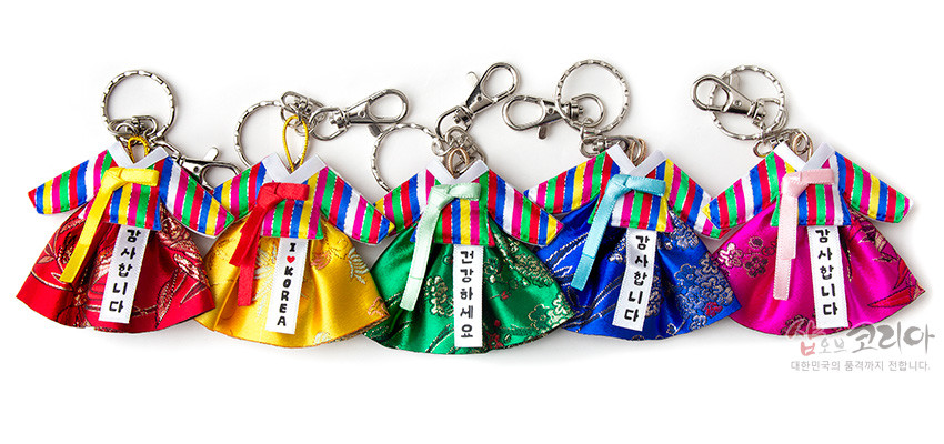 [텍스트: 감사합니다 / I ♥ KOREA / 안녕하세요 / 대한민국의 품격까지 전합니다] 색동 소매와 고름이 돋보이는 비단 한복 모양 열쇠고리, 오방색과 전통 꽃무늬 직물이 조화를 이룬 디자인