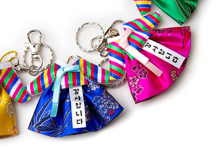 [텍스트: 감사합니다] 색동 소매와 고름이 돋보이는 비단 한복 모양 열쇠고리, 오방색 줄무늬와 전통 꽃문양 짜임, 금속체인 장식 구성