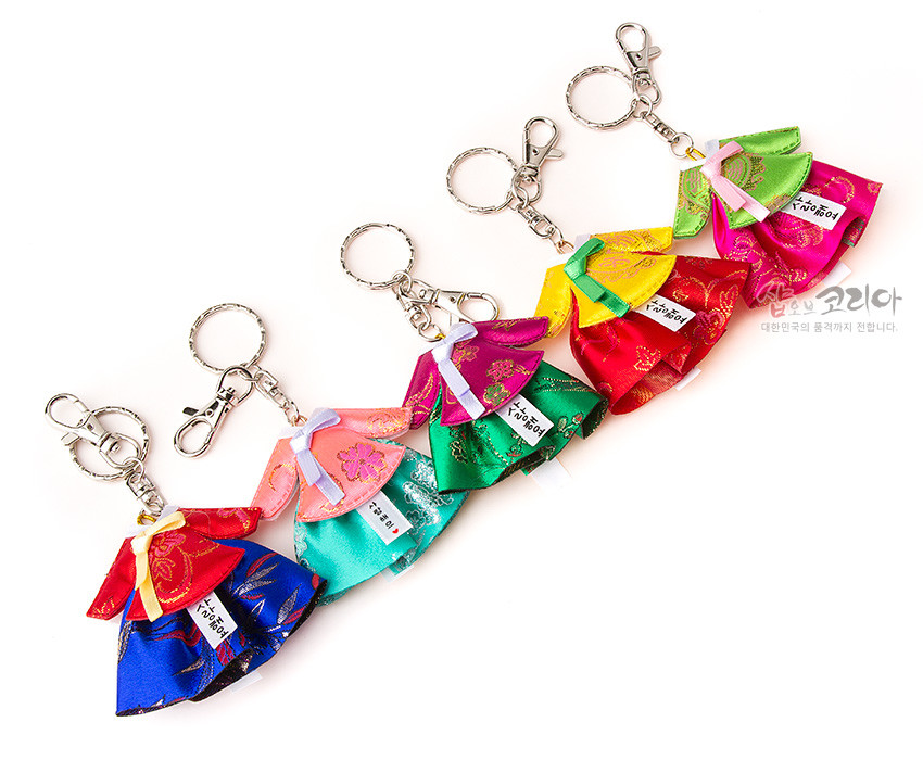 [텍스트: 샵오브코리아 대한민국의 품격까지 전합니다.] 비단 소재로 제작된 미니 당의 한복 열쇠고리, 금속 체인과 고리 장식, 화려한 색상과 전통 꽃문양 직조가 돋보이는 디자인