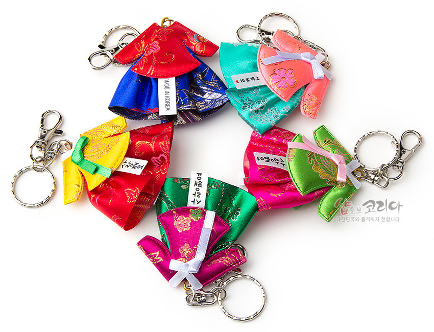 [텍스트: MADE IN KOREA, 샵오브코리아 대한민국의 품격까지 전합니다] 비단 소재에 금색 꽃문양을 직조한 미니 당의 한복 모양 열쇠고리, 다양한 색상의 대비와 금속 체인·고리 장식 특징