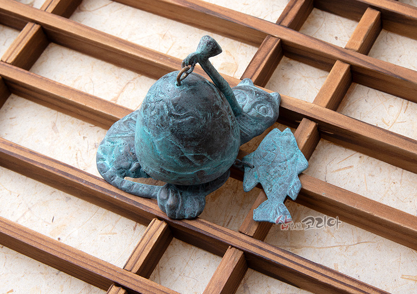 [텍스트: 샵오브코리아] 청동 재질에 청록색 산화 효과를 준 호랑이 형상 문종과 물고기 모양 추 장식, 나무 격자 위 배치된 인테리어 소품 연출