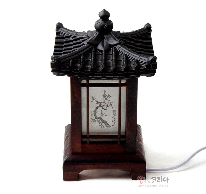 [텍스트: 샾오브코리아 대한민국의 품격까지 전합니다.] 짙은 갈색 목재 받침과 기와 지붕 형식, 창호 구조 안 반투명 한지에 수묵 사군자 매화 문양이 배치된 전통 좌등 디자인