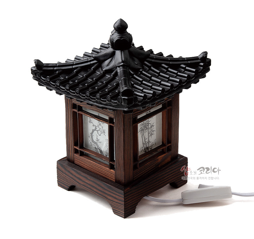 [텍스트: 샵오브코리아 대한민국의 품격까지 전합니다.] 흑색 기와 지붕과 짙은 갈색 나무 기둥 구조, 사면에 흑백 사군자 수묵화가 인쇄된 한지창으로 구성된 전통 좌등 형식 조명 디자인