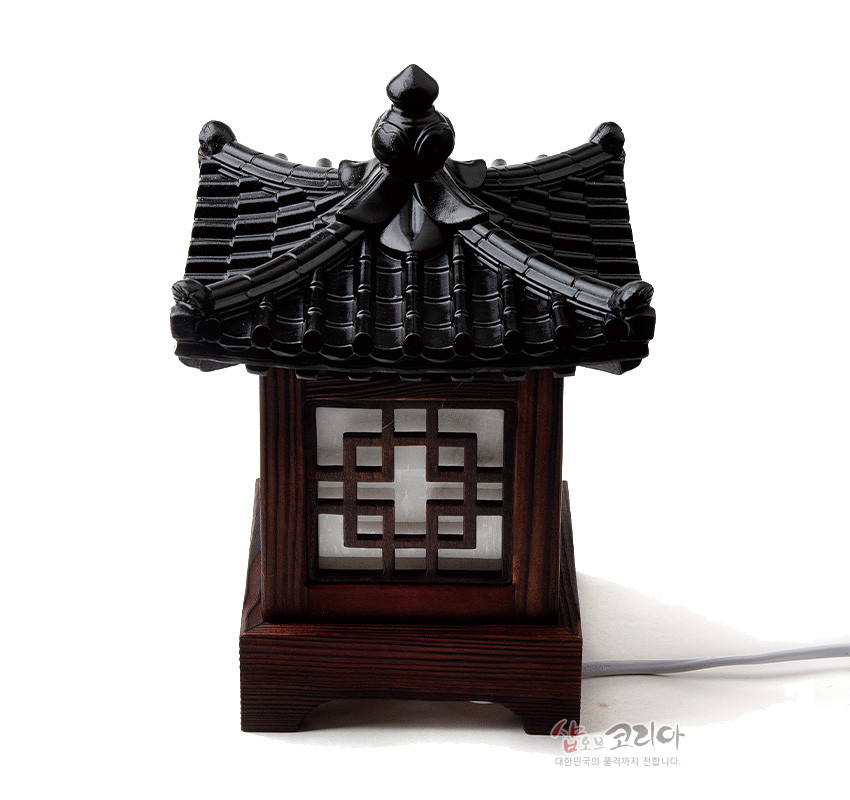 [텍스트: 샵오브코리아 대한민국의 품격까지 전합니다.] 짙은 흑색 기와 지붕과 짙은 갈색 목재 몸체 조합, 반투명 창호지 질감 창에 정(井)자 완자문 창살이 장식된 전통 좌등형 조명소품 이미지