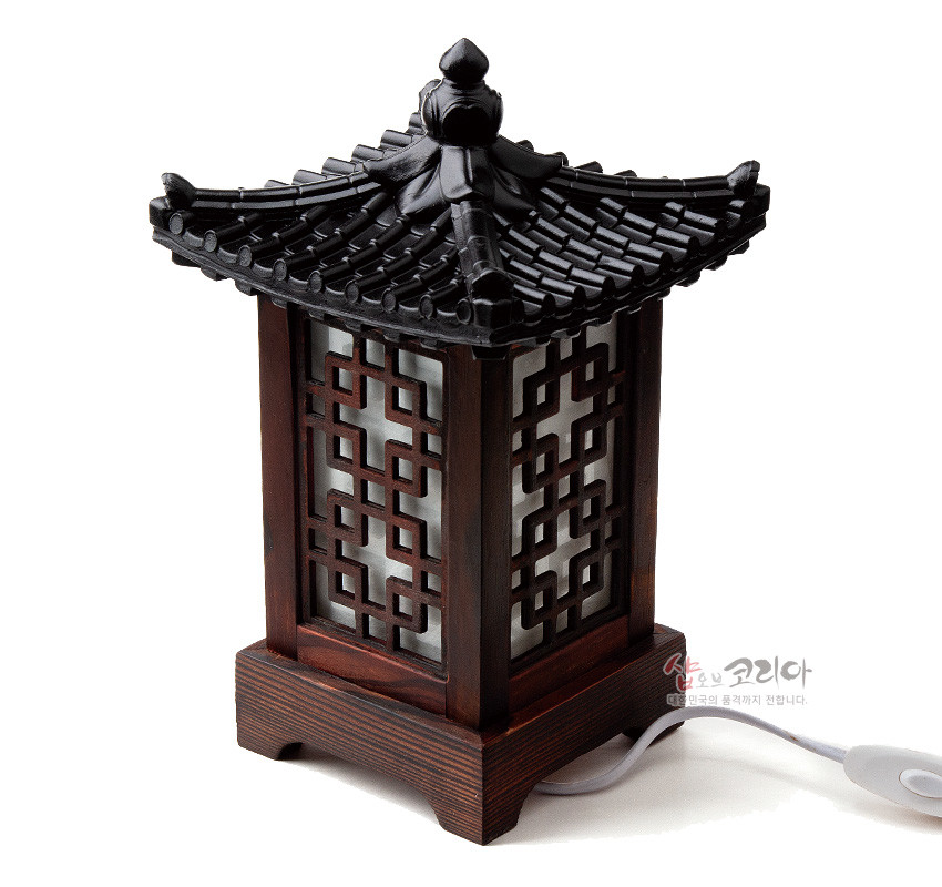 [텍스트: 샵오브코리아 대한민국의 품격까지 전합니다.] 짙은 갈색 목재와 전통 기와 지붕 형식, 유백색 한지 배경 위 완자문 격자 장식이 조화를 이룬 미니 좌등 이미지 설명