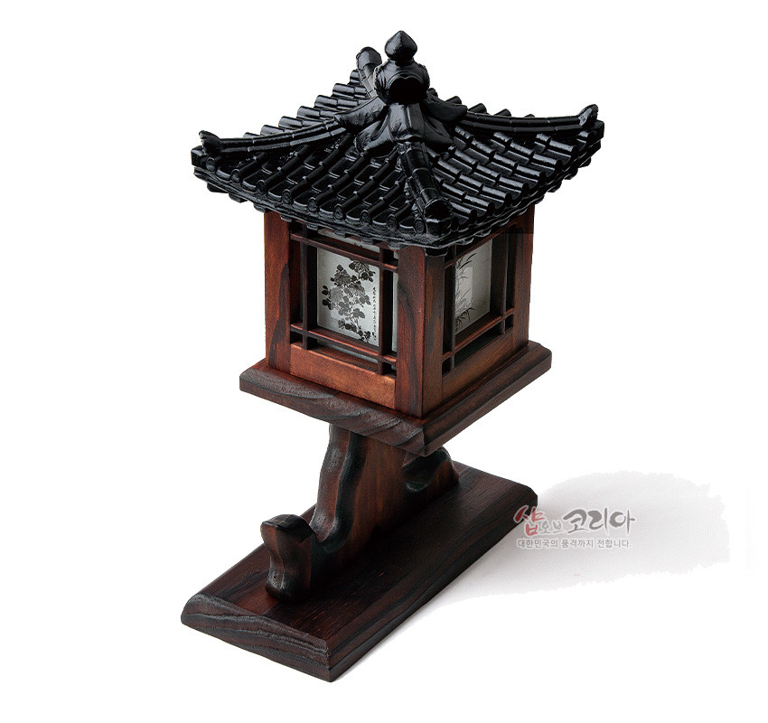 [텍스트: 샵오브코리아 대한민국의 참문화를 전합니다.] 흑색 기와지붕과 짙은 갈색 목재 구조, 반투명 창호면의 사군자 수묵화 문양이 조화를 이룬 전통 좌등 장식소품 이미지 설명