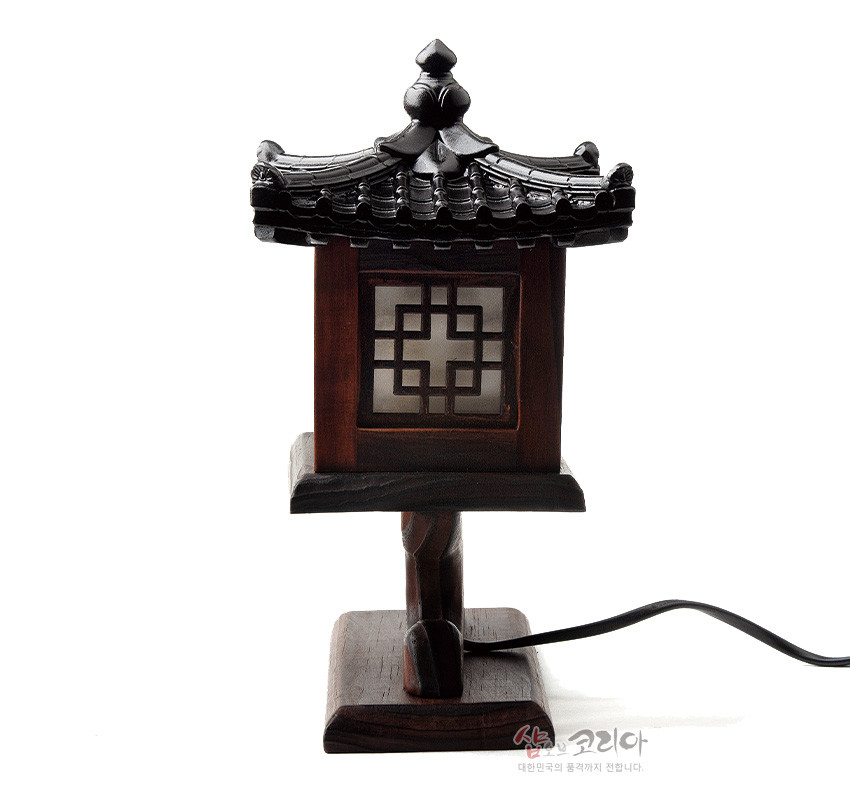 [텍스트: 샵오브코리아 대한민국의 품격까지 전합니다.] 짙은 갈색 목재와 흑색 기와 지붕, 반투명 창호에 완자 격자 문양을 더한 전통 누각 형식 좌등 디자인