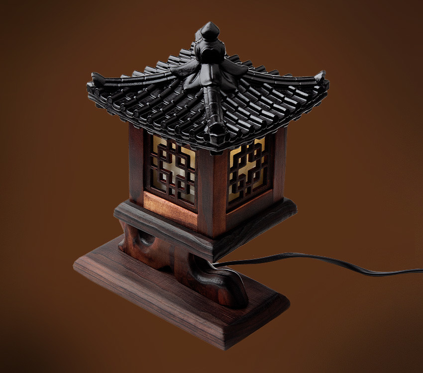 짙은 갈색 원목과 흑색 기와형 지붕으로 구성된 미니 좌등, 반투명 창호에 완자 격자 문양을 넣은 전통 누각형 조명 소품 모습