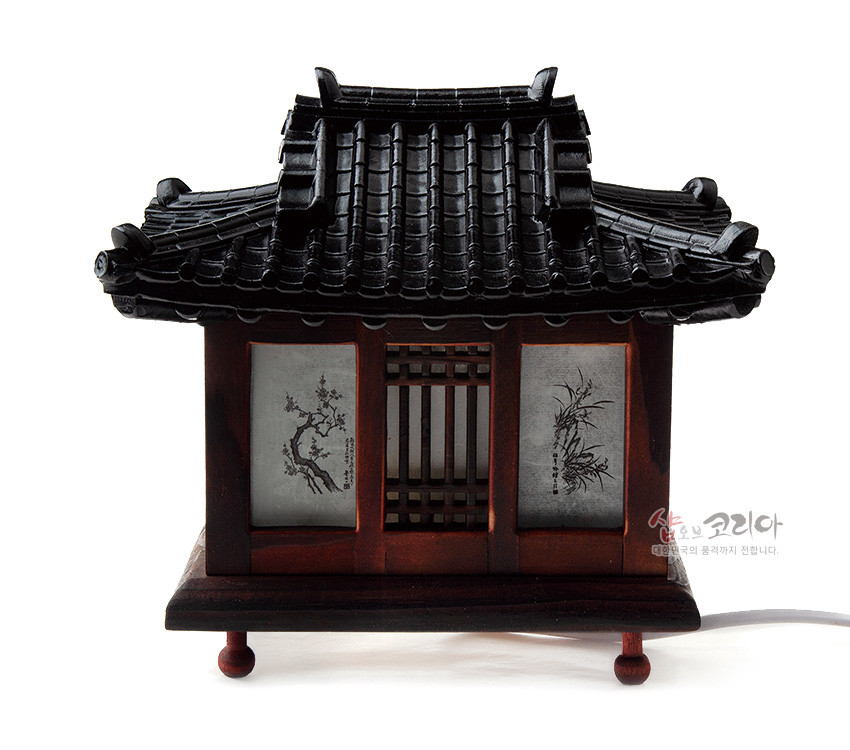 [텍스트: 샵오브코리아 대한민국의 품격까지 전합니다.] 짙은 흑색 기와지붕과 짙은 갈색 목재 구조, 창호지에 수묵 매화·대나무 문양이 들어간 전통 기와집 형태 소형 좌등 장식