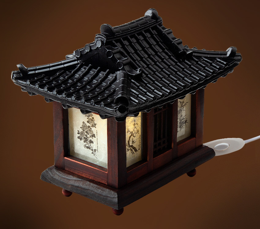 [텍스트: 없음] 짙은 흑색 기와지붕과 짙은 갈색 목재 구조, 반투명 창호지에 수묵화 매화·대나무 문양이 그려진 전통 기와집 형태 좌등 장식