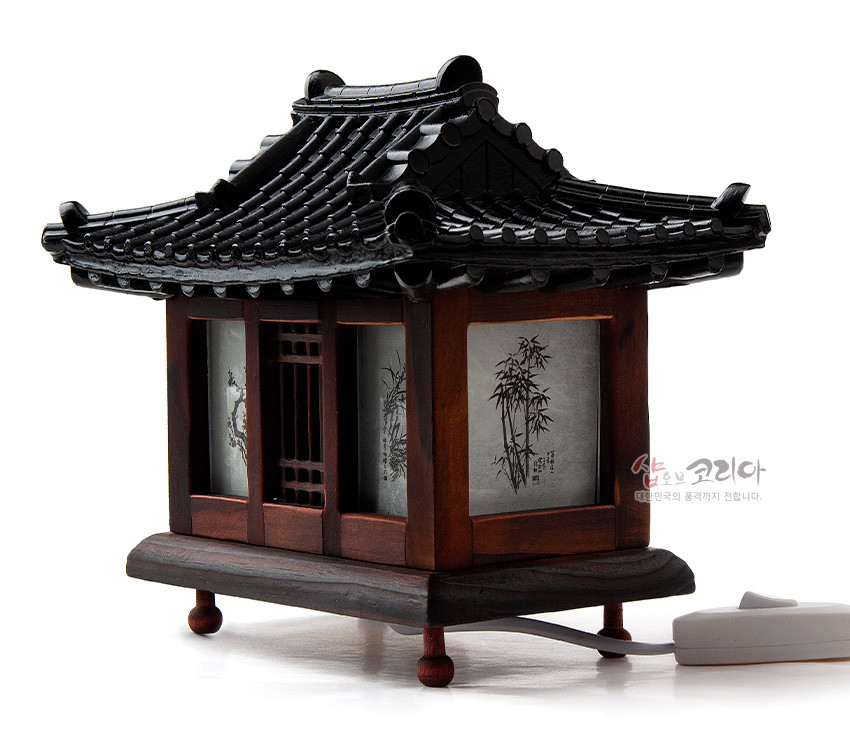 [텍스트: 샵오브코리아 대한민국의 품격까지 전합니다.] 흑색 기와지붕과 붉은 갈색 목재 구조에 반투명 창호지, 수묵화 대나무와 산수 문양이 둘러진 전통 기와집 형태 미니 좌등 장식