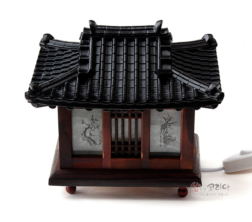 [텍스트: 샵오브코리아 대한민국의 품격까지 전합니다.] 흑색 기와지붕과 짙은 갈색 목재 구조, 창호지에는 수묵 매화·대나무 문양이 그려진 전통 기와집 형태 좌등 디자인
