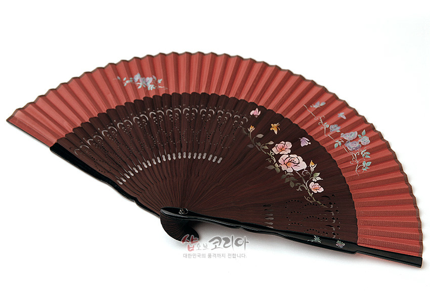 [텍스트: 샵오브코리아 대한민국의 품격까지 전합니다.] 갈색 실크 선면에 분홍·흰 목단과 꽃가지 수공 채색, 검은 나무살 위 레이저 타공 무늬가 조화를 이룬 접이식 부채 이미지 설명