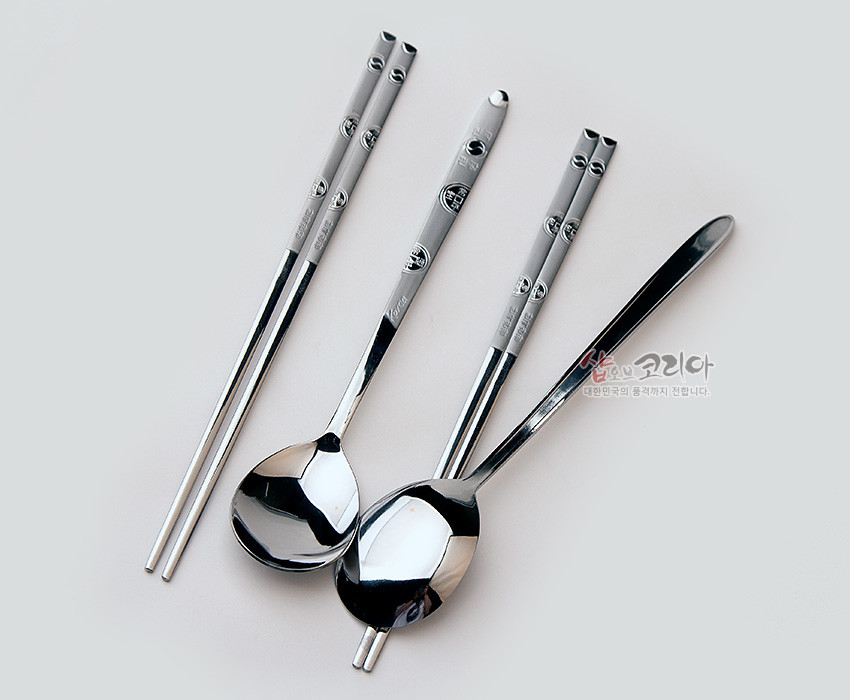 [텍스트: 샵오브코리아 대한민국의 품격까지 전합니다.] 은색 스테인리스 재질, 손잡이에 엽전 양각 문양과 한글 글자가 새겨진 한국식 숟가락·젓가락 2인 세트 모습