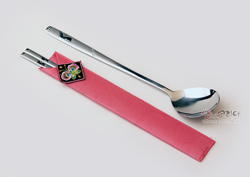 [텍스트: 샵오브코리아 대한민국의 품격까지 전합니다.] 분홍 비단 수저집과 자수 나비 장식, 광택 있는 금속 숟가락과 젓가락으로 구성된 전통 수저 세트 이미지