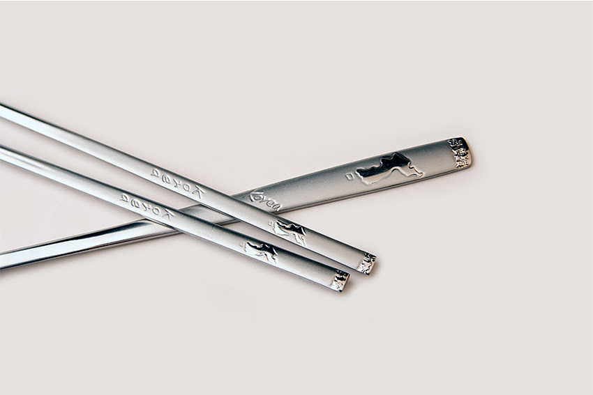 [텍스트: Korea] 무광 실버 톤 금속 재질의 숟가락과 젓가락, 손잡이 부분 한반도 지도 양각 문양과 영문 각인 장식 디테일 강조된 구성