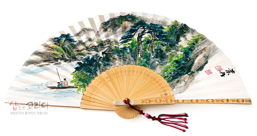 [텍스트: 샵오브코리아 / 대한민국의 품격까지 전합니다.] 백색 한지에 수묵채색 청록산수화와 낚시 인물 문양, 대나무 살과 붉은 매듭 술 장식의 합죽선 접부채 이미지