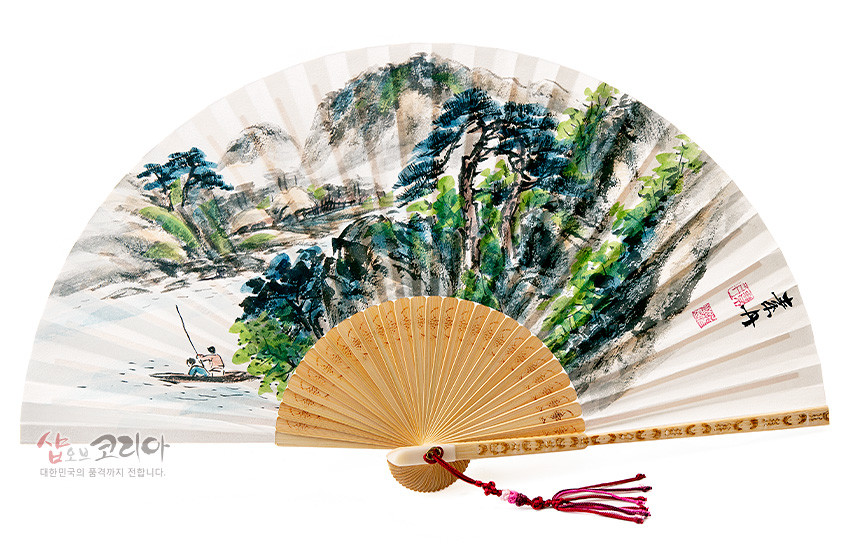 [텍스트: 샵오브코리아 대한민국의 품격까지 전달합니다.] 백색 한지에 청록 수묵 산수화와 낚시하는 인물 문양이 그려진 합죽선, 대나무 살과 끝부분 음각 장식, 붉은 매듭 술 장식 접부채 모습