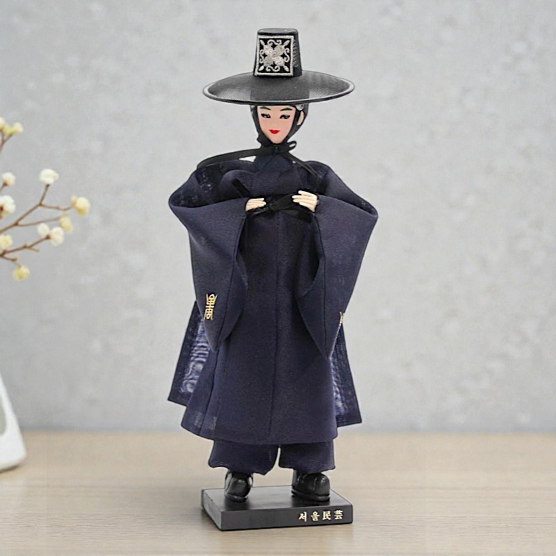 [텍스트: 서울민예] 짙은 남색 한복과 전통 갓을 착용한 저승사자 인형, 섬세한 비단 직물과 단정한 선비 복식 표현