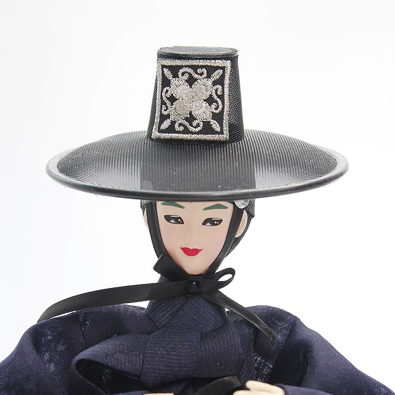 [텍스트: 없음] 검은 사뿐갓과 흰색 자수 문양 정자관 장식, 남색 비단 한복과 매듭 리본이 조화를 이루는 저승사자 한복 인형 모습