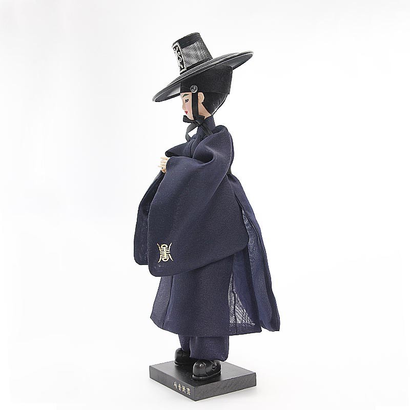 [텍스트: 서울특별시] 짙은 남색 비단 한복과 갓을 쓴 저승사자 인형, 하단 받침대의 각인과 소매의 금색 문자 자수 장식, 단정한 측면 실루엣 연출