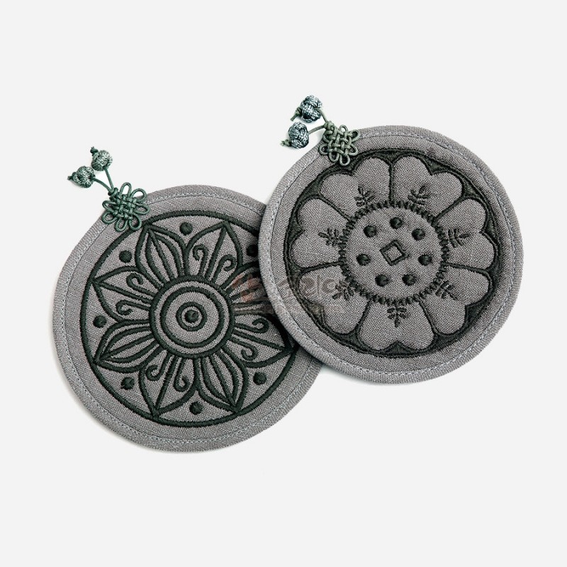 회색 천 재질에 고구려·백제 수막새 연꽃 문양을 짙은 색 실로 자수한 원형 컵받침과 매듭 장식.