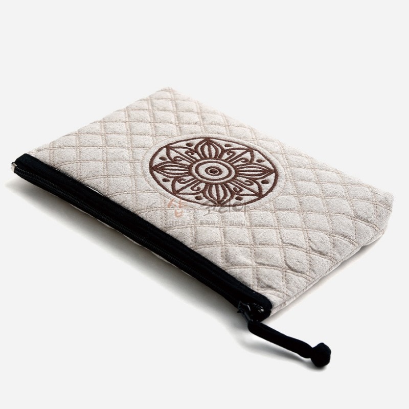 부드러운 백색 천에 누빔 기법을 더하고, 중앙에 갈색 고구려 수막새 문양 자수로 장식한 지퍼 파우치.