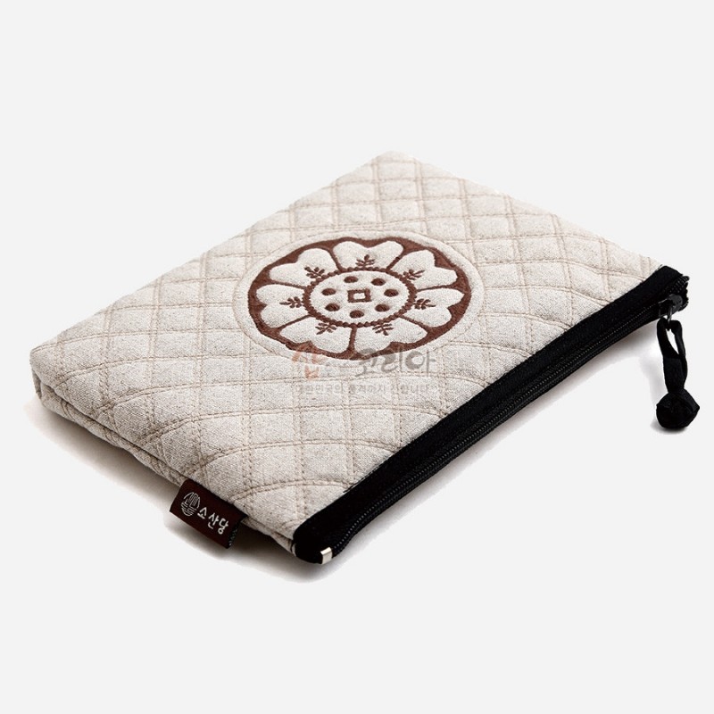 백색 누빔 천 소재에 갈색 백제 수막새 문양 자수와 검정 지퍼 장식이 특징인 파우치. 백색 누빔 천 소재에 갈색 백제 수막새 문양 자수와 검정 지퍼 장식이 특징인 파우치.