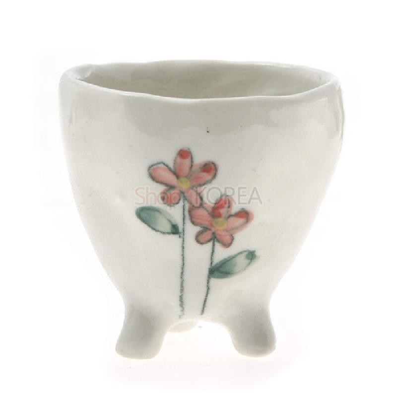 흰색 도자기로 만든 삼각 발 달린 소주잔, 연분홍 야생화와 초록 잎을 손그림으로 장식한 디자인.