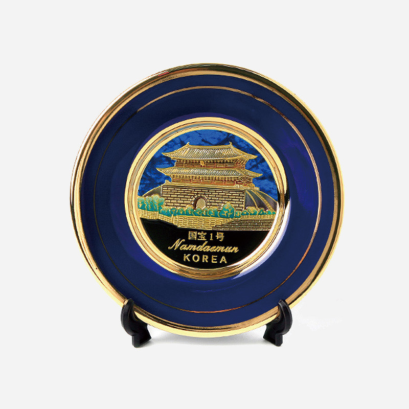 청색 바탕 위 금속 재질에 금장 남대문 전경을 양각으로 표현하고, 가장자리에 금색 띠 장식을 더한 원형 접시 장식.