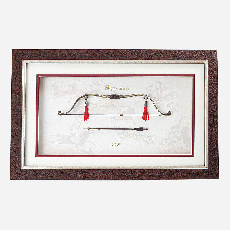 고급스러운 갈색 나무 액자 속 금속 재질 국궁과 화살 미니어처, 붉은 술 장식과 전통 수렵 문양 배경이 조화된 인테리어 액자.