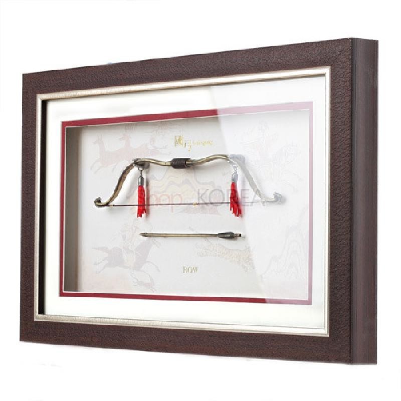짙은 갈색 나무 액자에 금속 미니어처 국궁과 화살을 입체 배치하고 붉은 술 장식과 전통 수렵 문양 배경이 조화를 이룬 장식 액자.