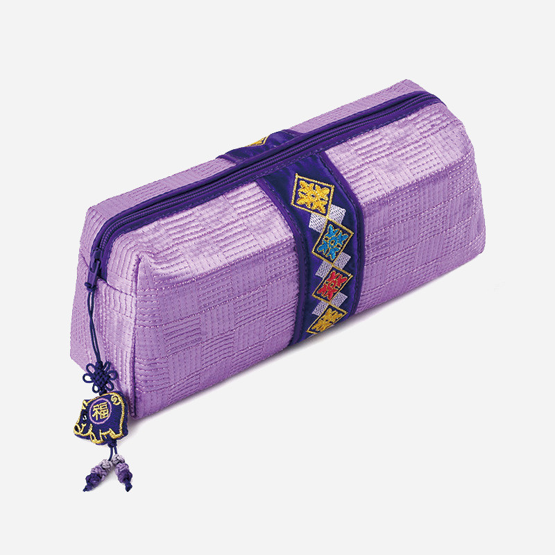 자색 누비 원단에 체크 패턴이 들어간 필통, 중앙에 다채로운 전통 자수 문양 장식과 복돼지 매듭 장식이 돋보이는 디자인.