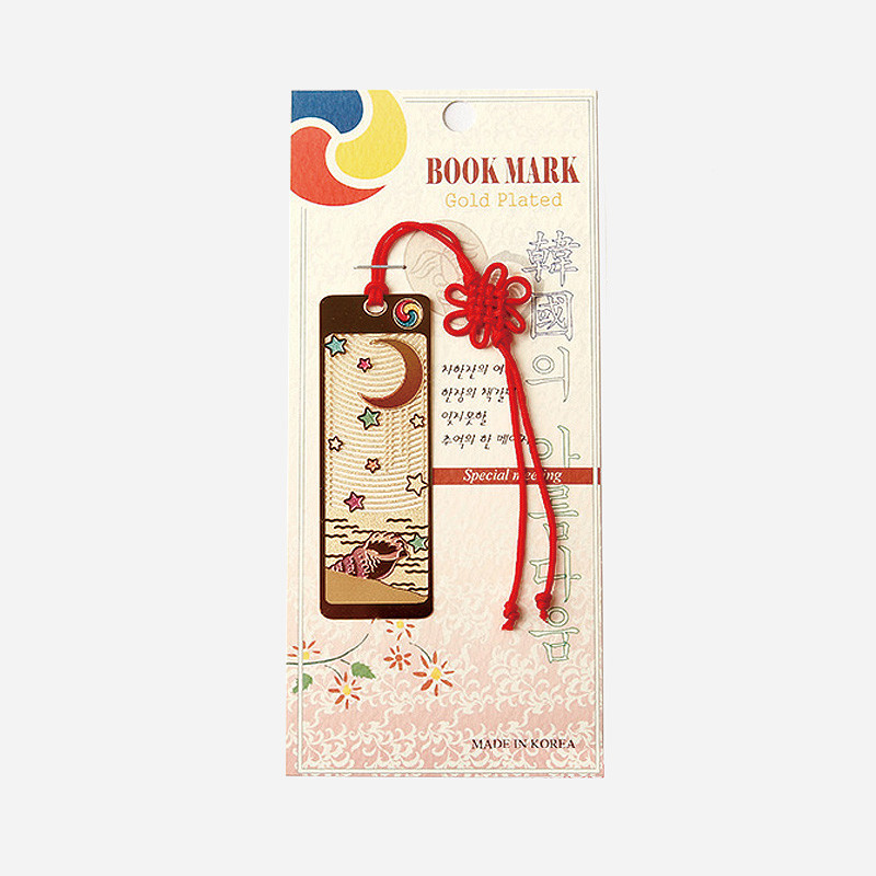 금장 금속 재질에 달과 고동, 별 문양이 양각된 직사각 책갈피와 붉은 전통 매듭 장식 끈이 조화된 디자인.