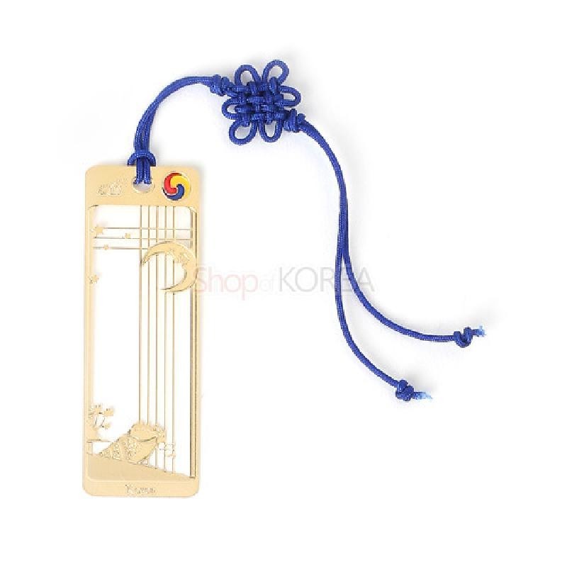 금장 금속 재질에 달과 고동, 별 문양을 오픈워크로 표현하고 상단 태극 문양과 파란 전통 매듭끈 장식이 특징인 책갈피.