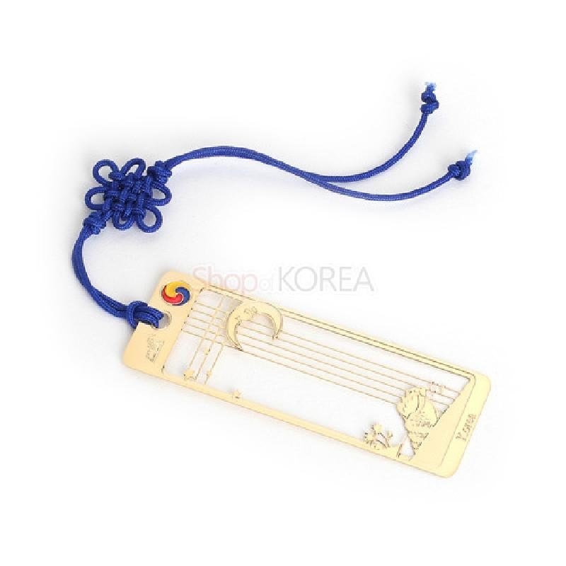 금속 재질의 금장 책갈피에 달과 고동 문양을 섬세하게 투각하고, 상단에 태극 문양과 파란색 전통 매듭끈을 더한 디자인.