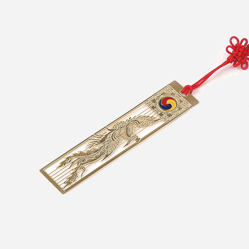 금속 재질에 정교한 봉황 문양을 금장으로 새기고, 상단에 태극 문양과 붉은 전통 매듭 끈을 더한 책갈피.