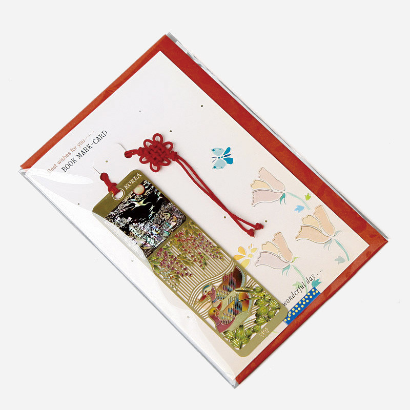 금속 바탕에 자개 상감으로 원앙과 꽃 문양을 넣고 붉은 전통 매듭 장식을 더한 책갈피.