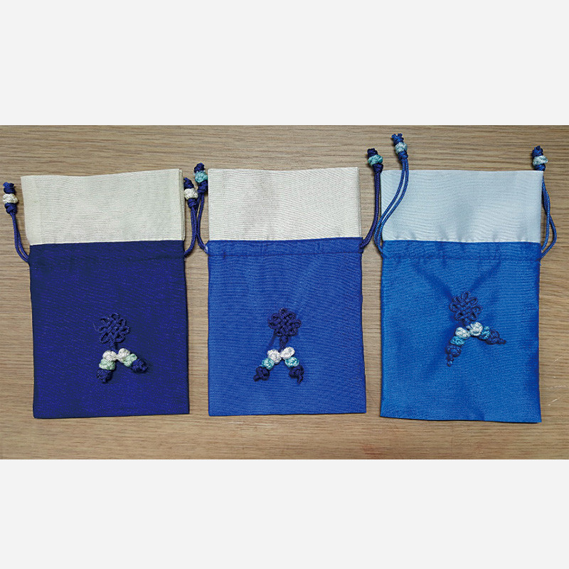 청색 계열 비단 소재로 제작된 매듭주머니, 상단 배색 처리와 중앙 전통 매듭 장식이 특징인 제품.