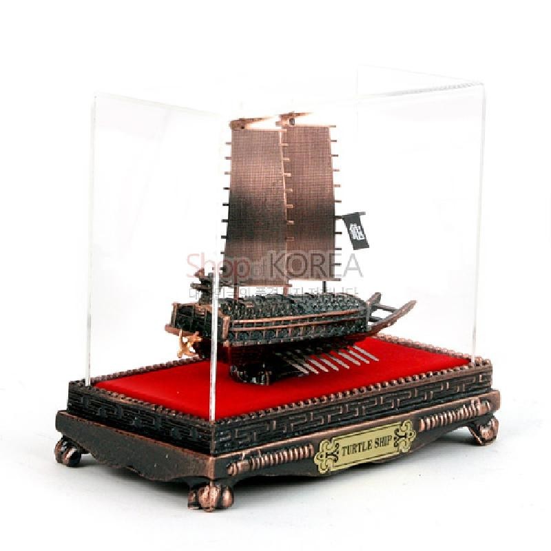청동색 금속으로 정교하게 제작된 거북선 모형과 붉은 천 바닥, 투명 아크릴 케이스가 조화를 이룬 장식품.