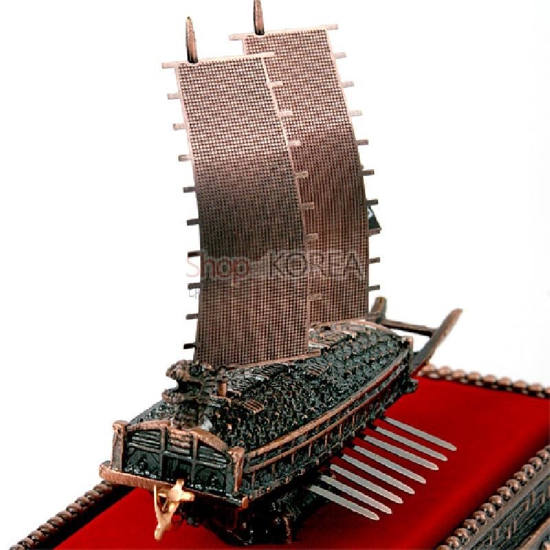 청동색 금속 재질로 표현된 거북선 모형, 세밀한 갑판과 돛 디테일, 붉은 받침대와 대비를 이루는 조형 장식.