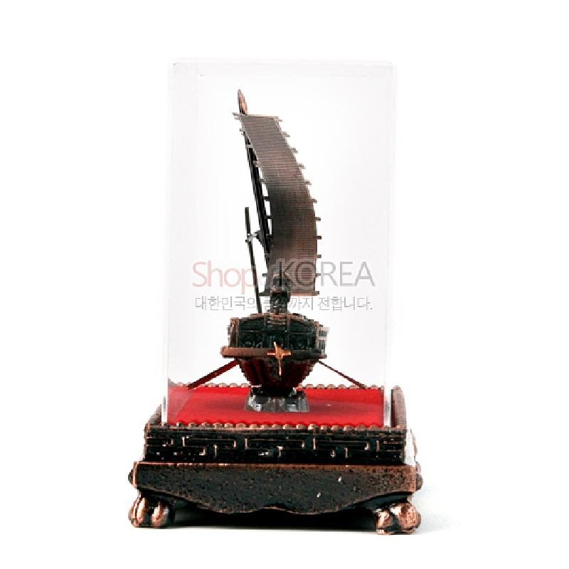 투명 아크릴 케이스와 적색 천 바닥 위 금속 재질의 동거북선 모형 장식.