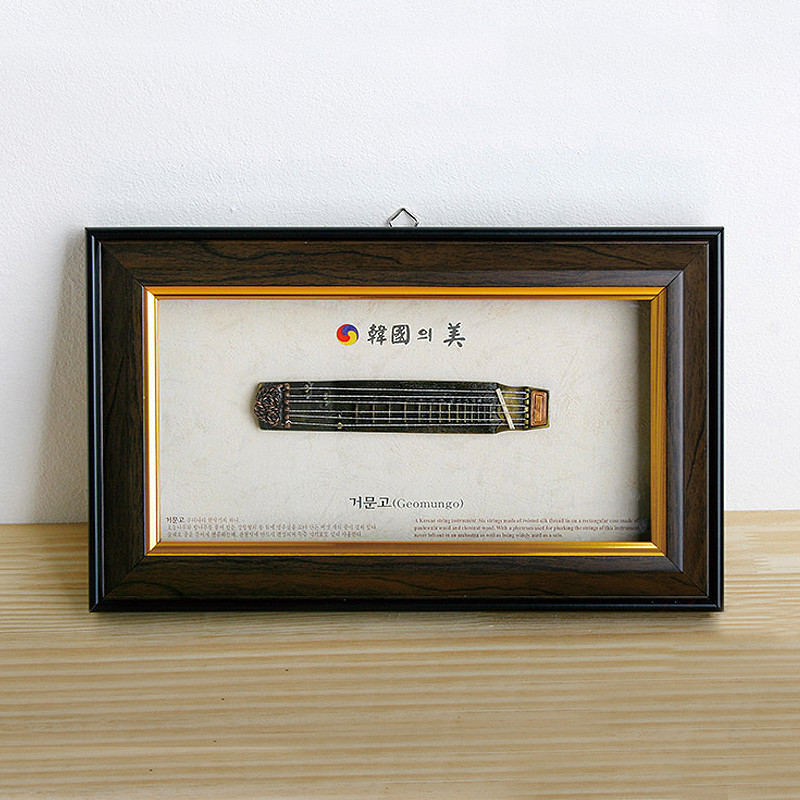 짙은 갈색 원목 느낌의 액자 속에 금속 재질 미니어처 거문고가 장식된 전통악기 모형 액자.