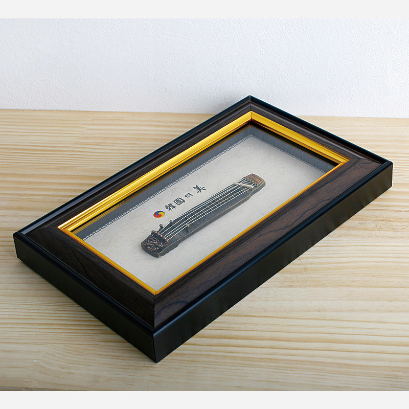 검은색과 짙은 목재색 액자에 금색 테두리를 두르고 금속 거문고 장식을 넣은 전통 악기 장식 액자. 검은색과 짙은 목재색 액자에 금색 테두리를 두르고 금속 거문고 장식을 넣은 전통 악기 장식 액자.