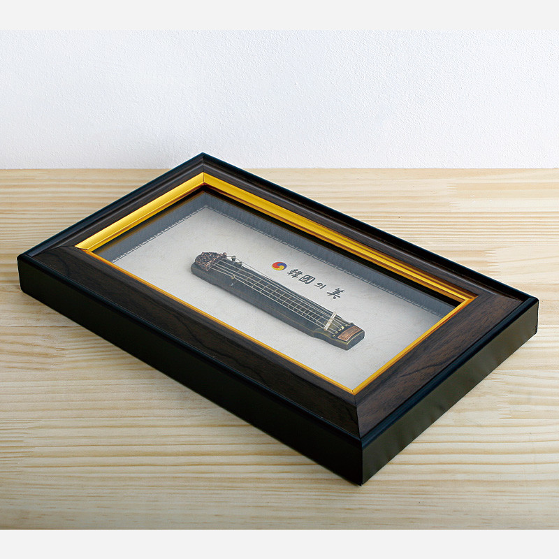 검은색 나무 질감 액자 속 미니어처 거문고 장식과 태극 문양, 금속 줄 세부 표현이 돋보이는 전통 악기 액자. 검은색 나무 질감 액자 속 미니어처 거문고 장식과 태극 문양, 금속 줄 세부 표현이 돋보이는 전통 악기 액자.