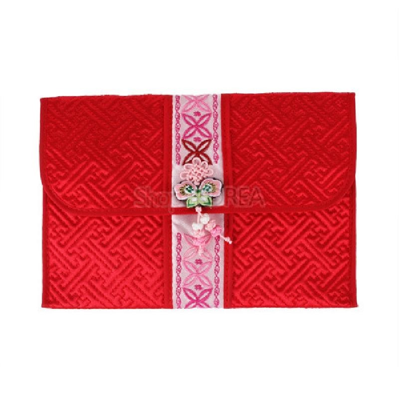 붉은 색 누비 원단에 전통 길상문이 양각된 지갑으로, 중앙에는 분홍빛 자수띠와 꽃·나비 문양 장식이 놓여 있다.
