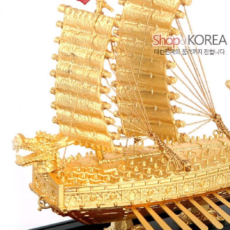 금속 재질의 황금빛 도금 처리와 용머리 장식, 세밀한 조각 문양과 돛대·노 구조가 특징인 거북선 모형.