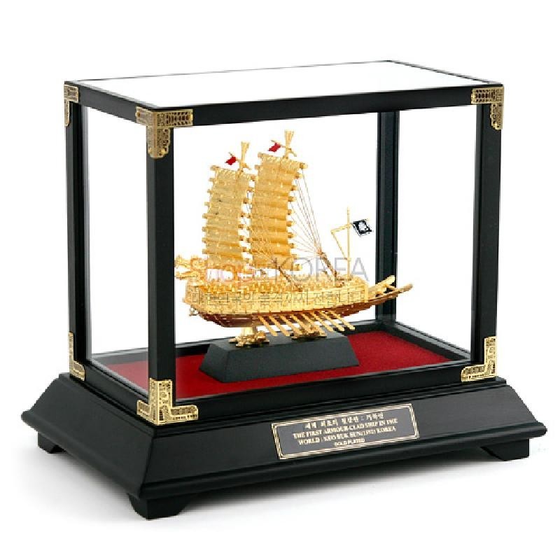 금속 재질의 황금빛 거북선 모형과 검정·적색 대비 받침대, 유리 쇼케이스 형태의 장식품.